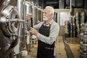 Mature male Engineer in Brewery looking at beer in a glass